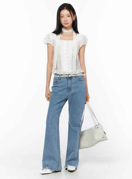 Puff Sleeve Shirred Blouse with Scarf IU519 in white, full-body front view on model holding white bag, puff sleeves, button-front, ruffled hem, scarf at neck, paired with flare jeans and belt.