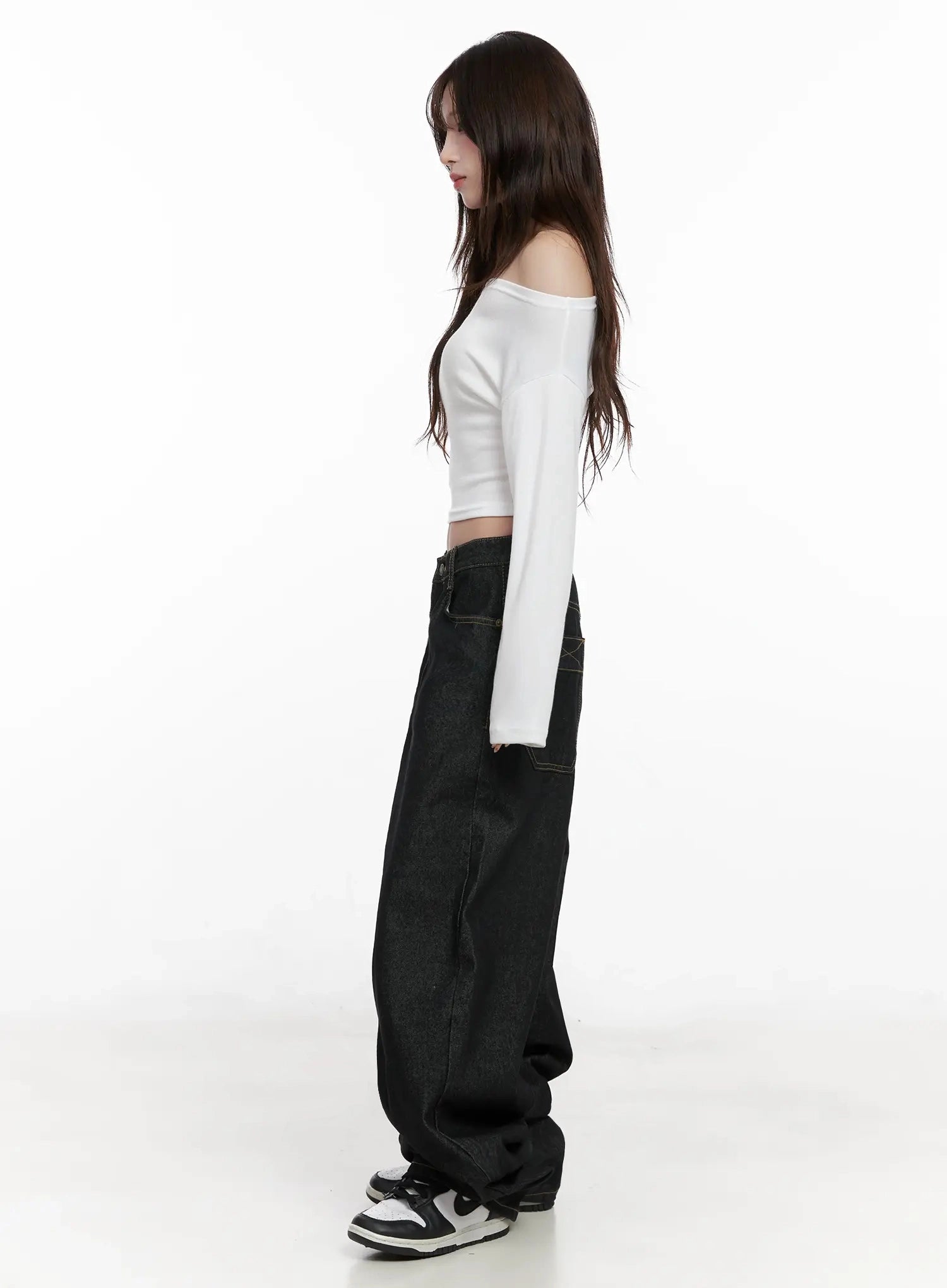 Halo Wide Leg Stitch Detail Jeans IN514 in black, side full-body shot on model, long wide-leg silhouette with floor-grazing hem, paired with white off-shoulder crop top and chunky sneakers.