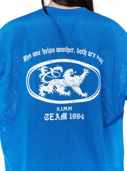 Oversized Mesh Graphic Tee CU519 in Blue M/L, back graphic close-up on model, perforated mesh fabric texture, white distressed lion crest oval and K.I.M.M TEAM 1994 back print detail.