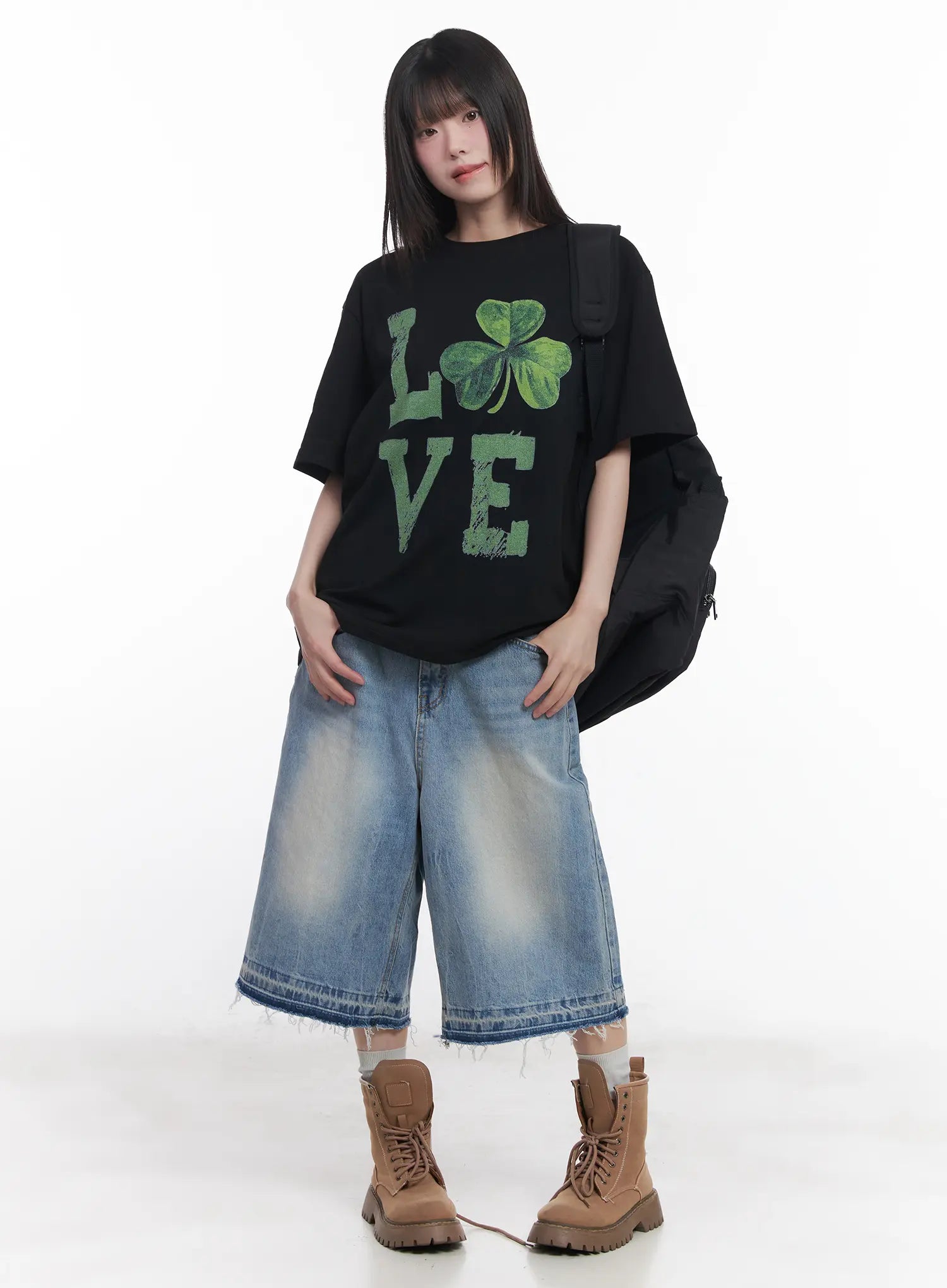Light Wash Vintage Jorts CU519 in blue, front full-body on model, wide-fit midi denim jorts with raw frayed hem, styled with black graphic tee, black shoulder bag, and tan combat boots.