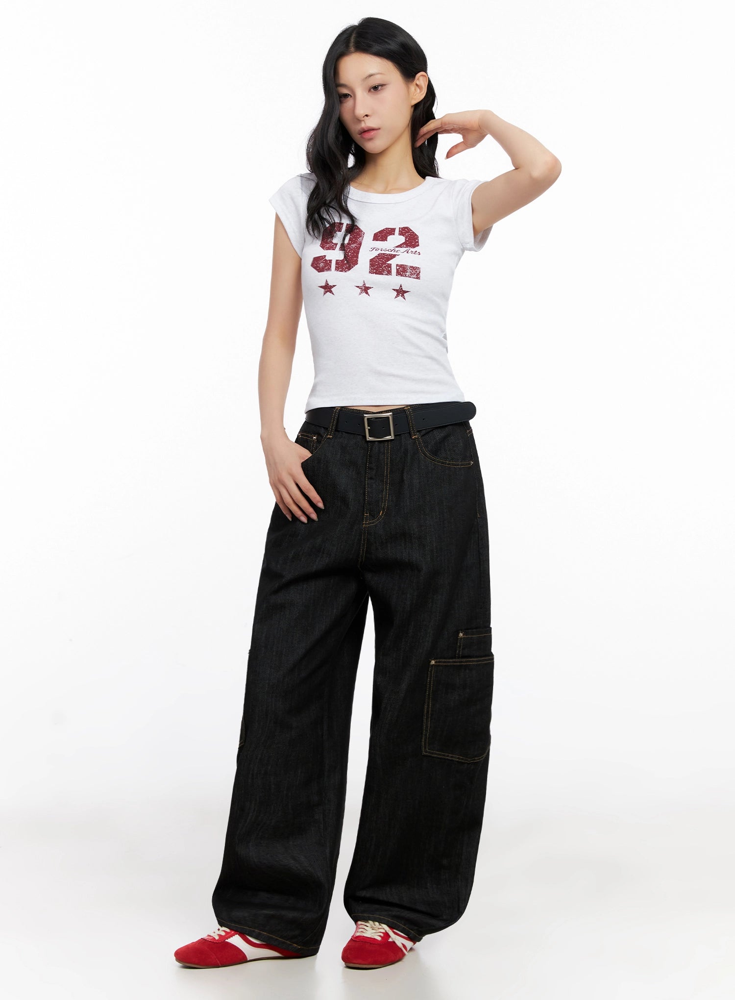 Dahee Wide-Leg Cargo Jeans IG508 in black, full-body three-quarter view on model with hand raised, belted waist, side cargo pocket prominent, wide-leg floor-length silhouette, styled with white graphic tee.