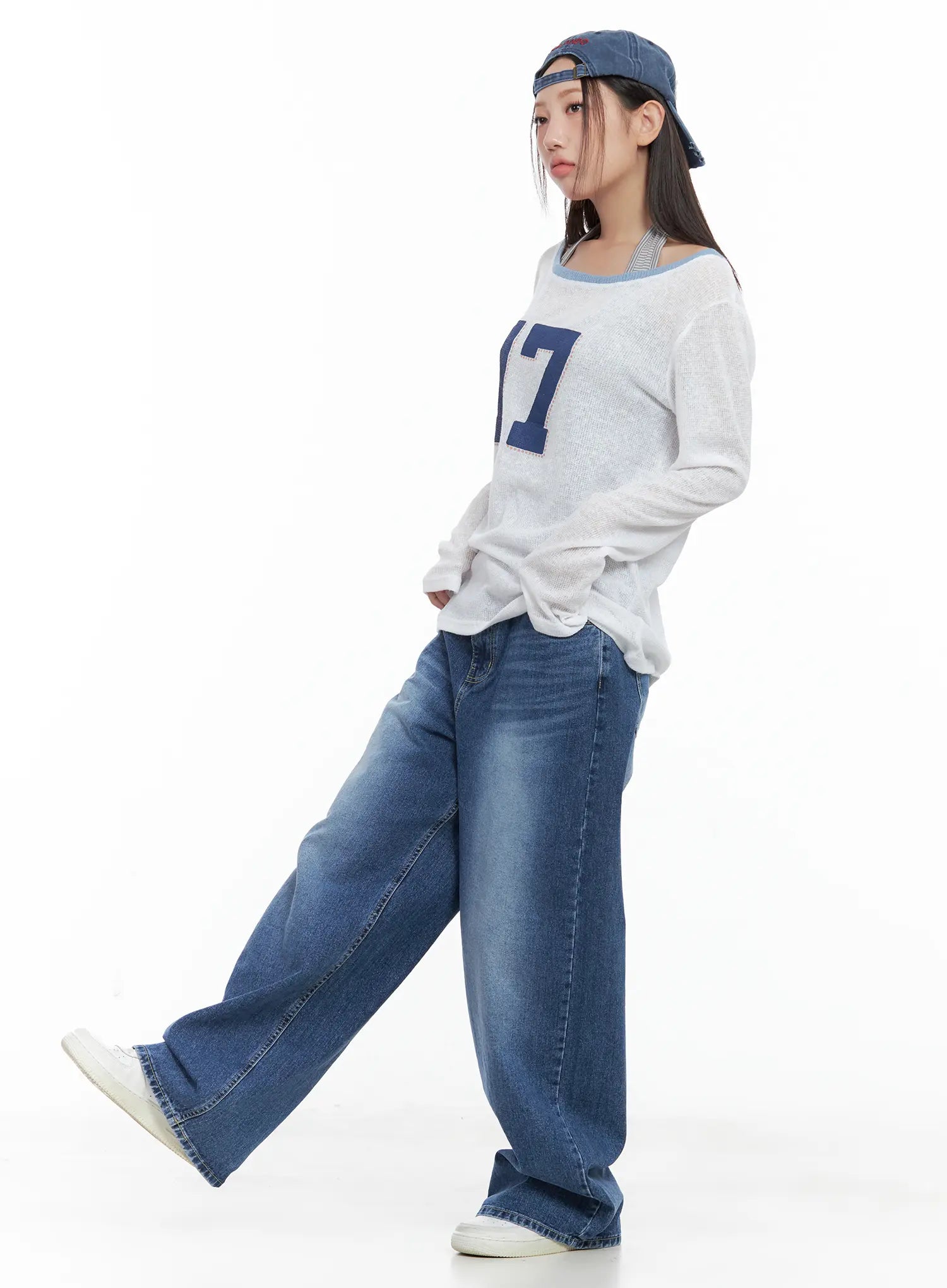Hayoung Washed Wide-Leg Denim Jeans CL509 in dark blue, three-quarter side view on model stepping forward, wide-leg drape and washed fade shown, paired with white graphic knit and cap.