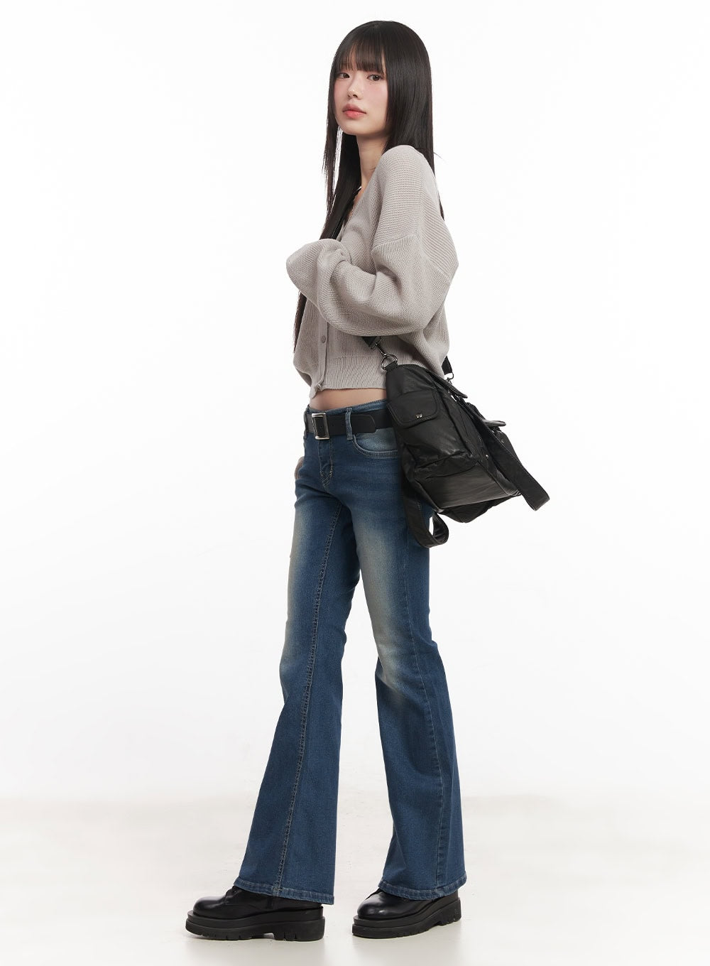 Rebecca Low-Waist Flared Jeans CM519 in dark blue, three-quarter side view on model in beige knit cardigan with black belt, carrying black bag, showing flare silhouette.