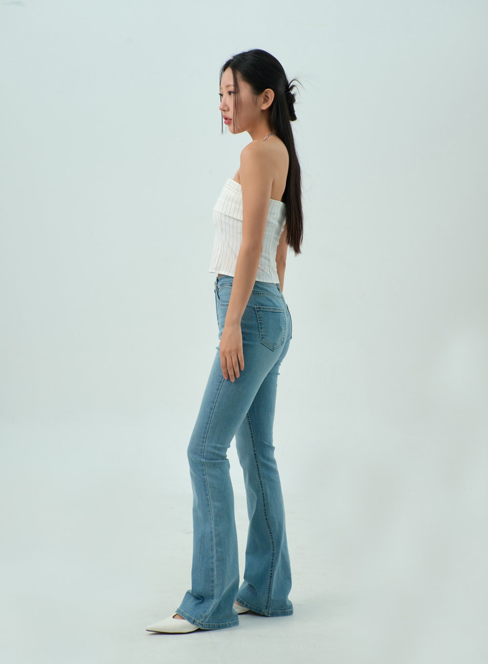Light Wash Bootcut Jeans CY330 in light blue, full side view on model, slim high-rise fit with visible back pocket, center seam running down flared bootcut leg, paired with white strapless top.