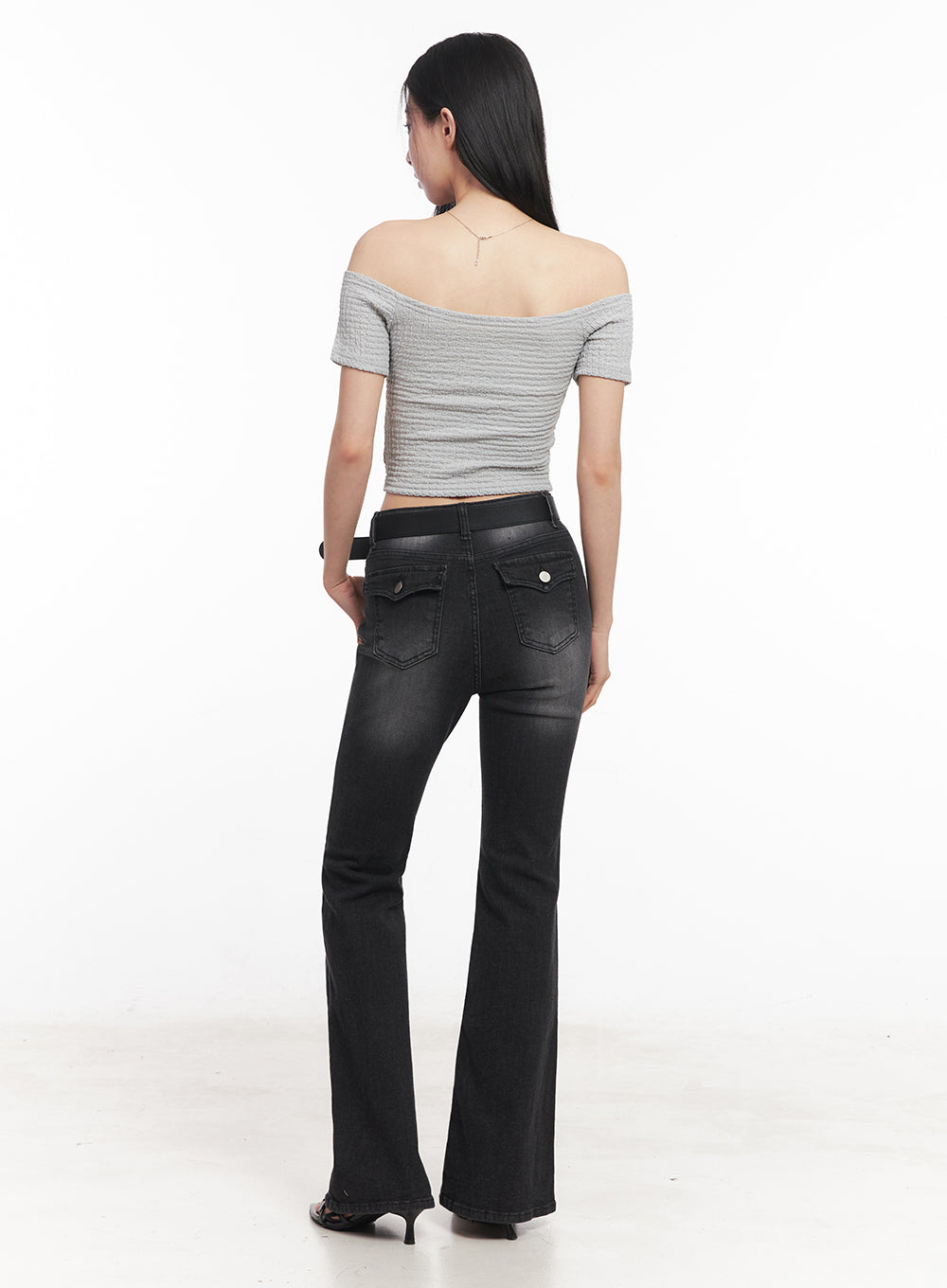 Lior Slim-Fit Bootcut Jeans IY516 in black, full-length back shot on model, washed bootcut denim with dual flap back pockets and silver button hardware, belted high-rise, grey crop top.