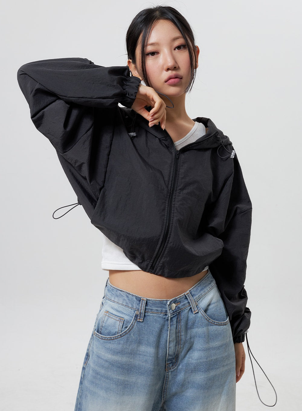 Low Rise Baggy Jeans CY324 in light blue, upper waist close-up on model with arm raised, low-rise front pocket and waistband detail visible, faded cotton denim, paired with black cropped jacket.