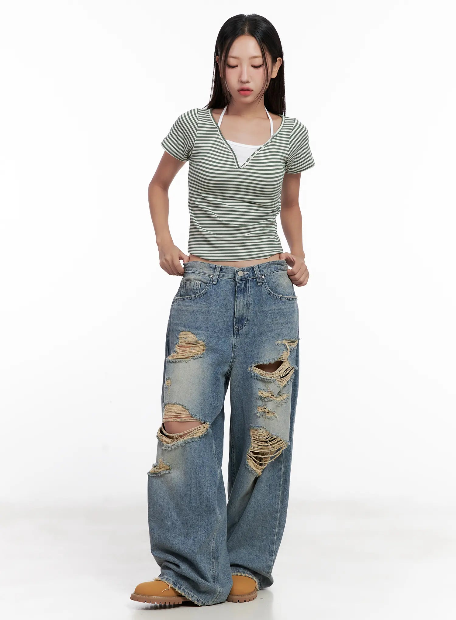Manon Washed Distressed Wide Jeans CL518 in blue, full-body front shot with model adjusting waistband, styled with green striped crop top, destroyed thigh openings prominently visible.
