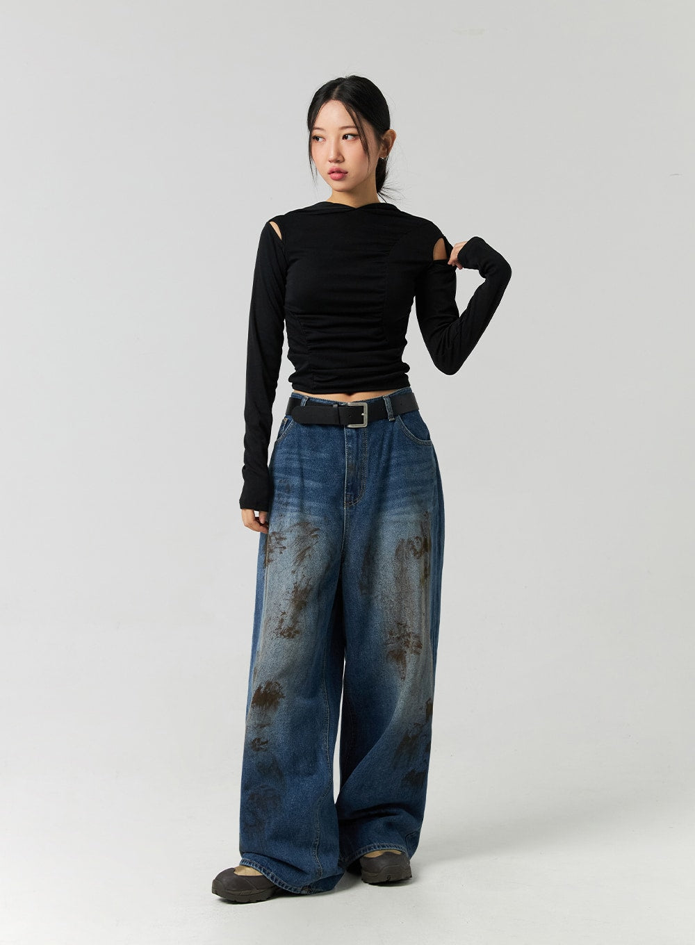 Street-Style Wide Fit Washed Jeans CO323 in Blue, full-body slight angle on model posing with hand raised, wide fit washed denim with brown abstract stain detail, belted at high waist.