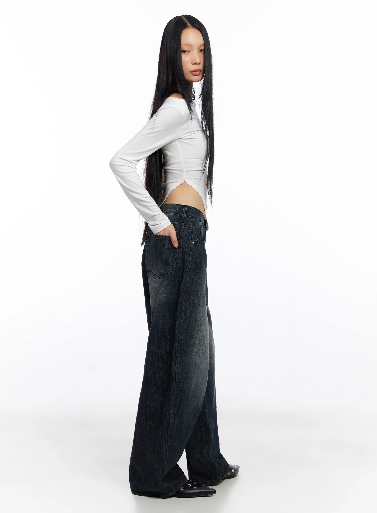 Minnell Vintage-Wash Wide-Leg Jeans IO517 in dark blue, side view on model in white off-shoulder long-sleeve top, hand on hip, showing low-rise waist and wide-leg sweep to floor.