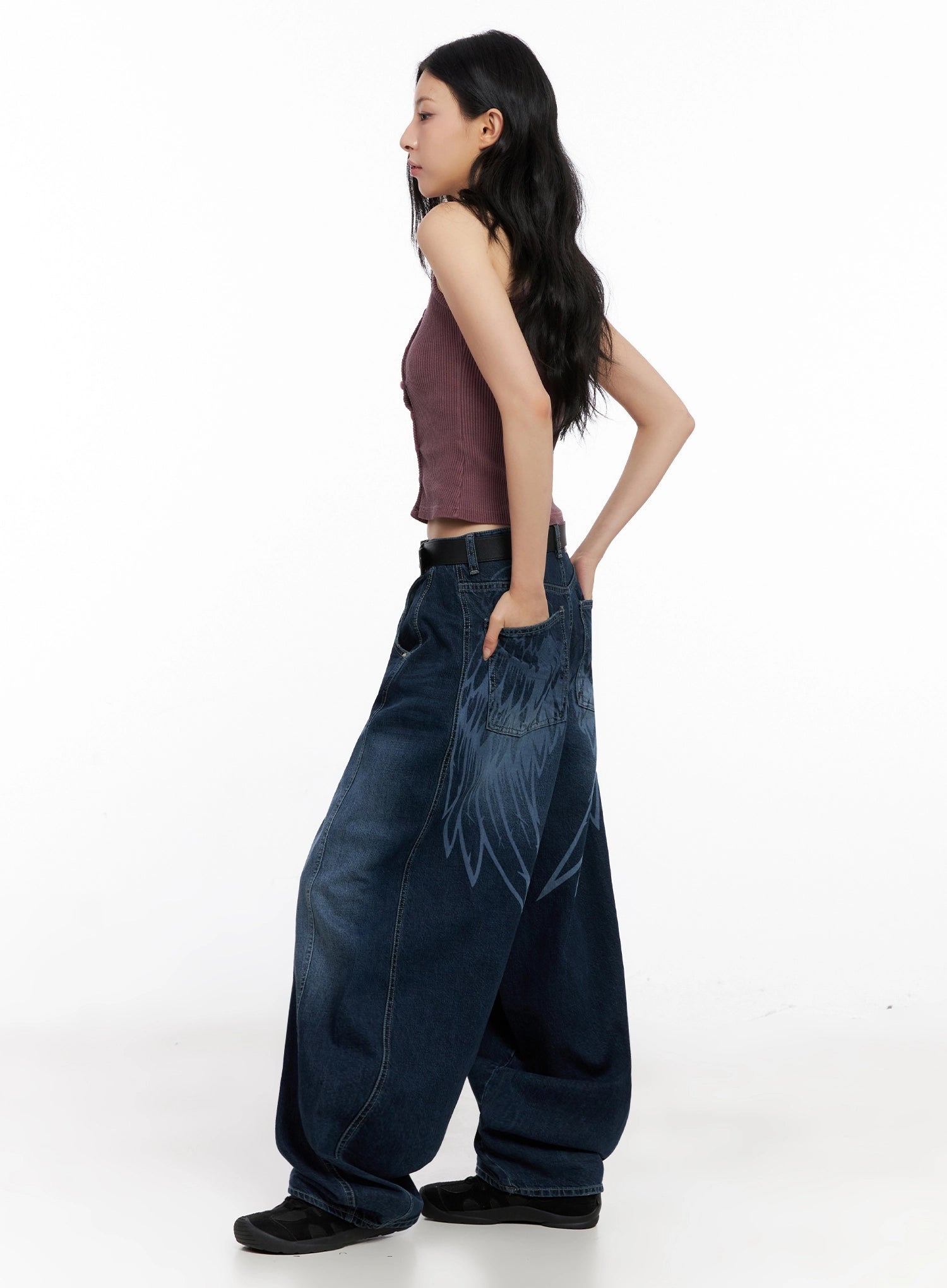 Sohee Angel Wing Print Wide-Leg Jeans IG508 in dark blue, side view on model, angel wing print visible along hip, exaggerated balloon-wide leg, paired with mauve crop tank and black belt.