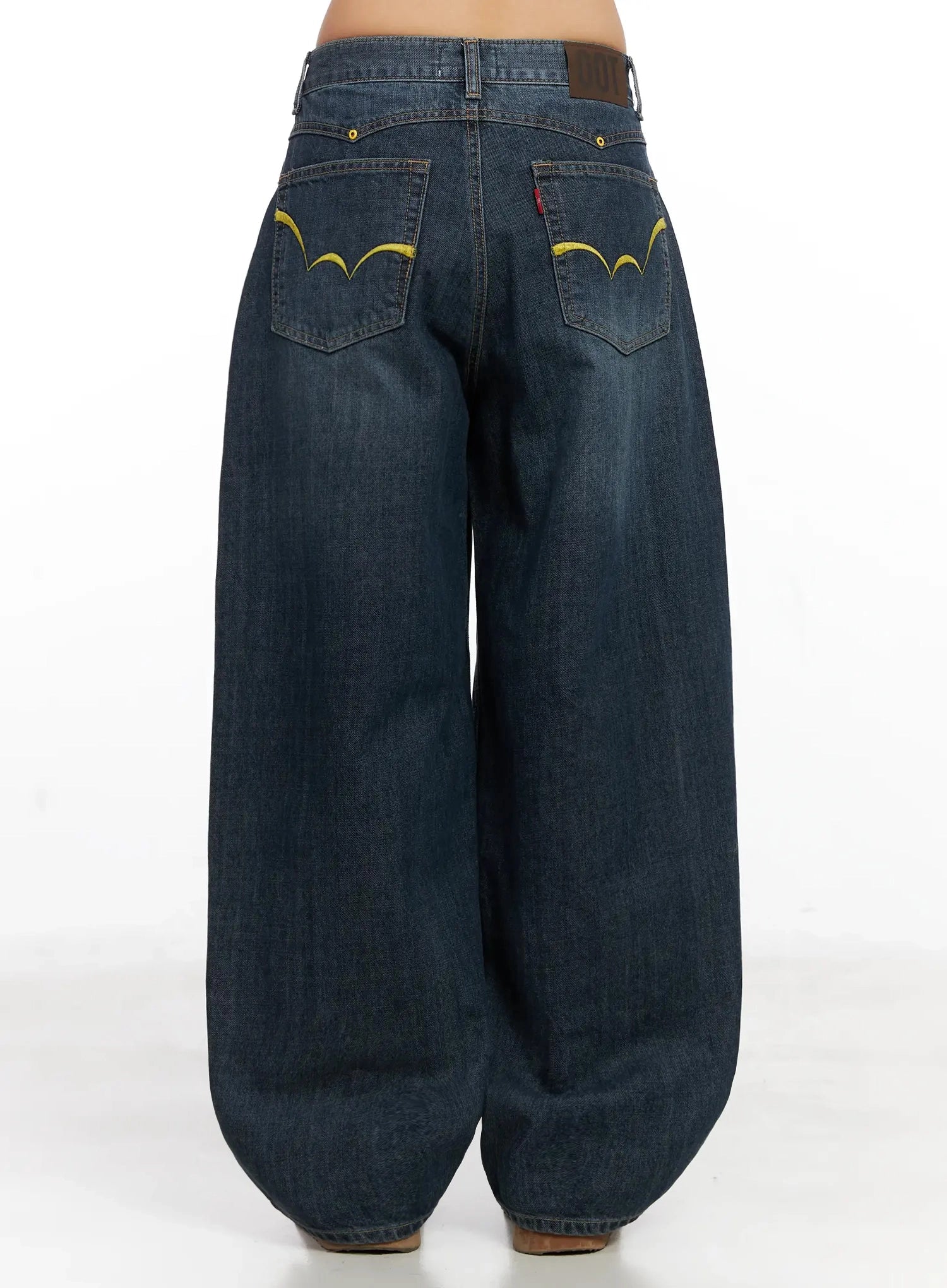 Regina Contrast Stitch Baggy Jeans IN528 in dark blue wash, back full-length product view, yellow contrast stitch arc embroidery on both back pockets, extremely wide baggy washed cotton leg silhouette.