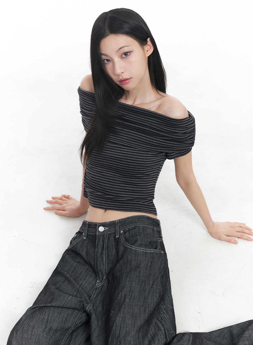 Lilli Wide-Leg Baggy Jeans IY516 in Black, editorial seated shot on model, waistband and front pocket close-up visible, low-rise denim with contrast stitching, paired with striped off-shoulder crop top.