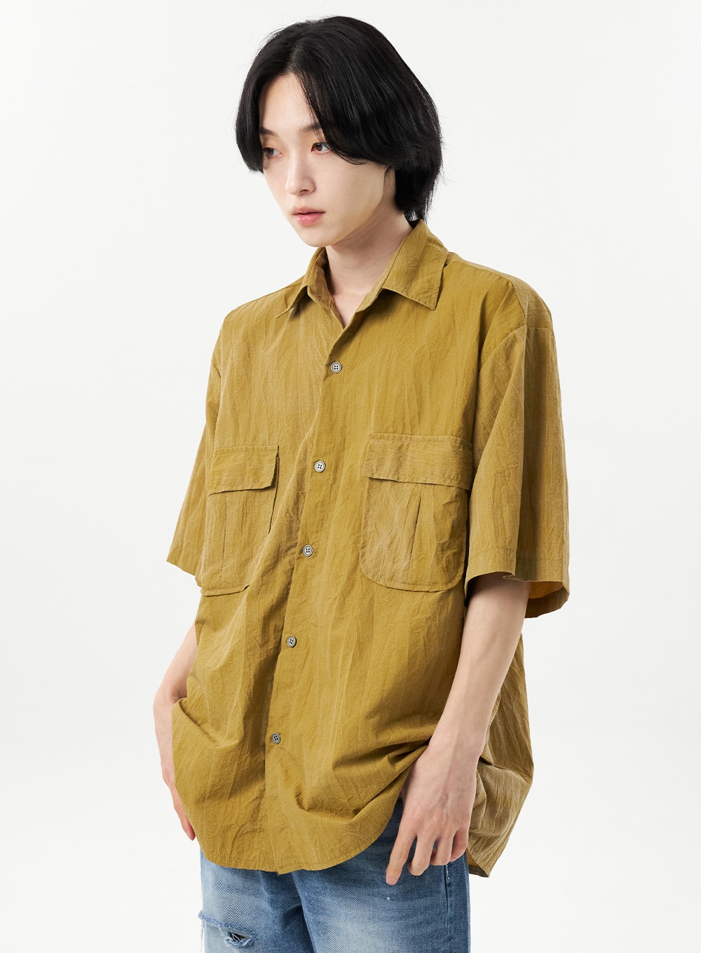 Ripped Jeans Unisex CU315 in mid blue, lower-body glimpse on male model in upper-body-focused shot, wide-fit denim with ripped hem visible, paired with mustard crinkle utility shirt, side angle.