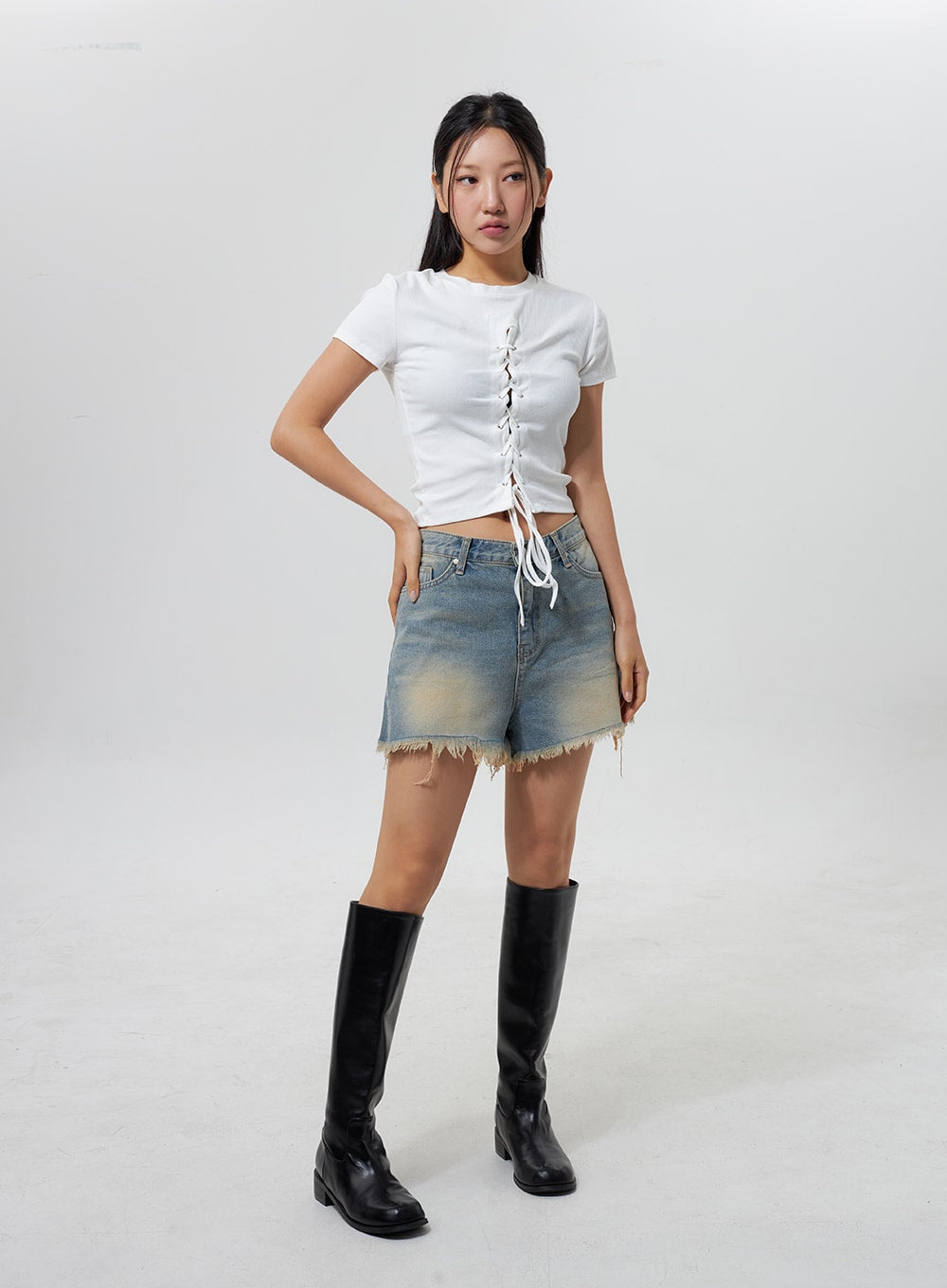 Mid-Rise Ripped Jeans CY323 in light blue, full-body front on model one hand on hip, washed denim shorts with distressed frayed hem, paired with white lace-up crop tee and tall black boots.