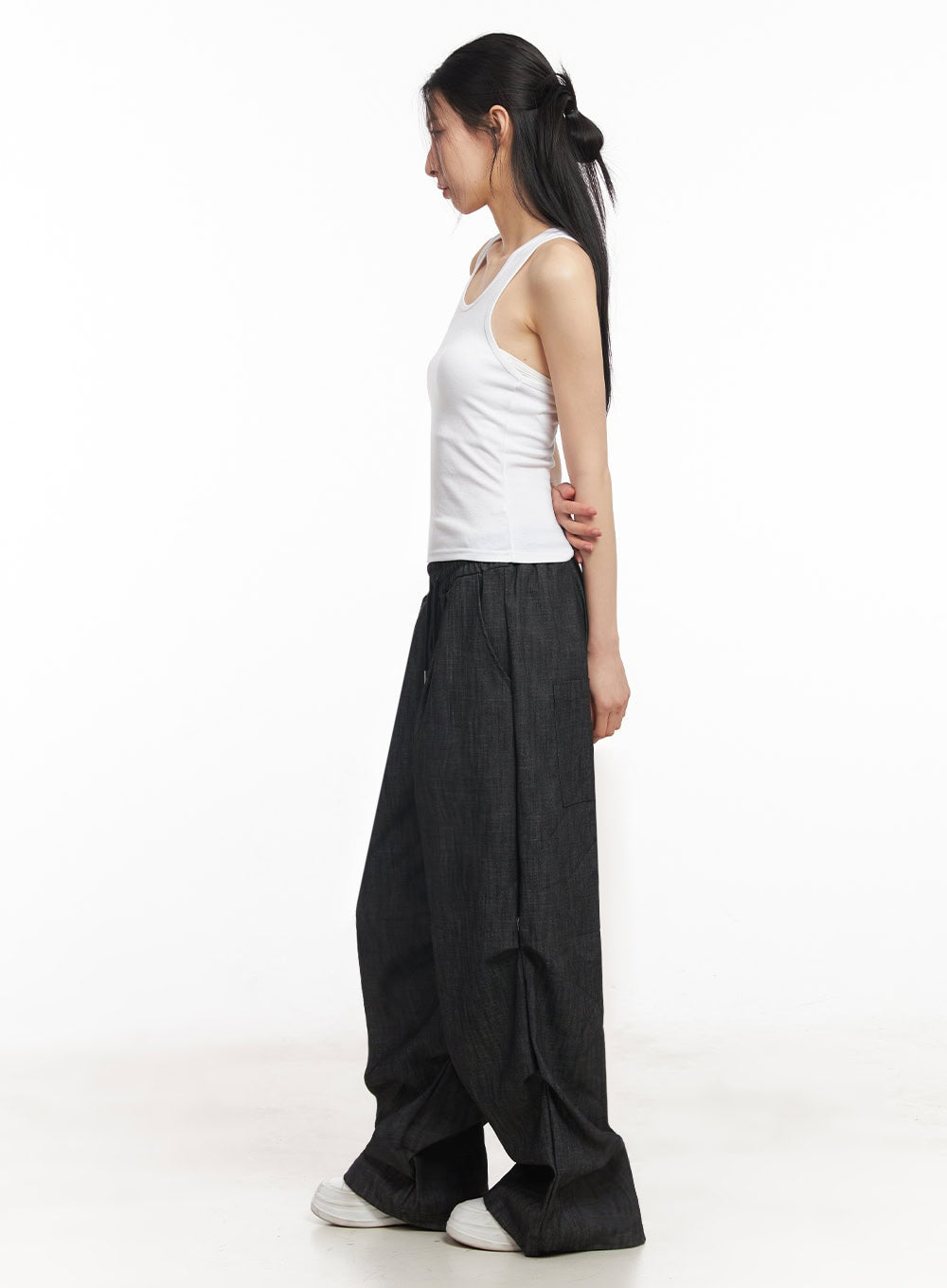 Pintuck Denim Sweatpants IY529 in black, side full-length view on model, wide-fit denim draping floor-length, elastic waist with drawstring, styled with white tank top and white sneakers.