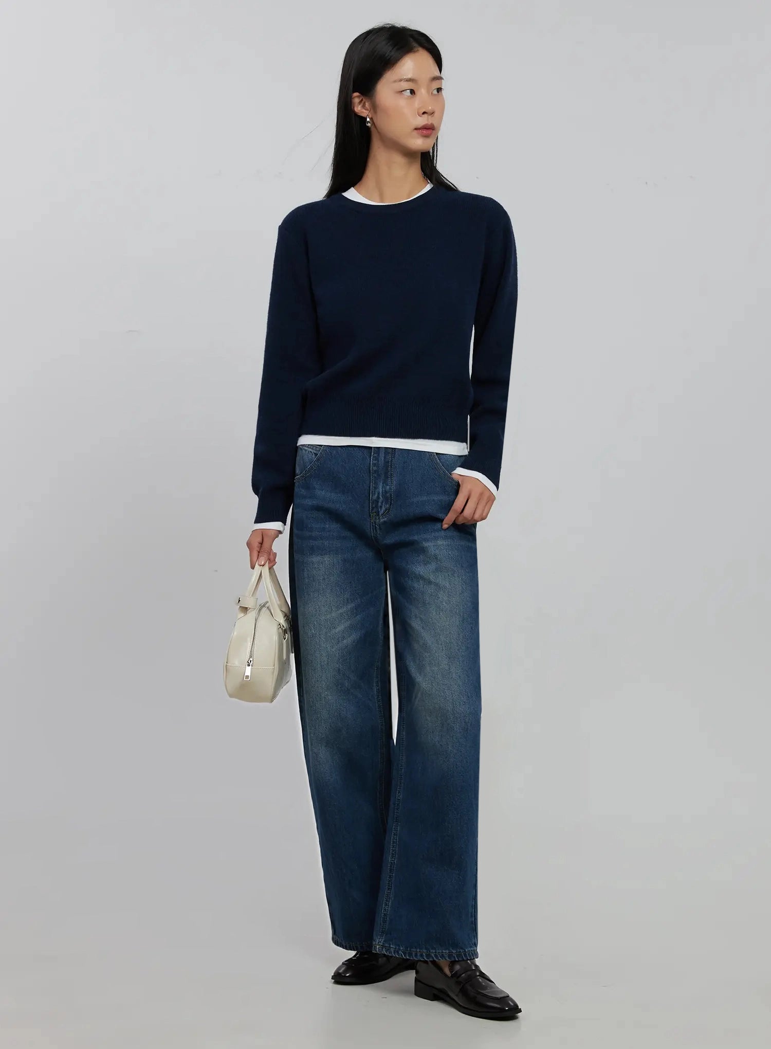 Alaina Wide Leg Jeans IJ508 in dark blue, full-length 3/4 angle on model holding white mini bag, paired with navy layered knit, wide-leg silhouette, loafer shoes.
