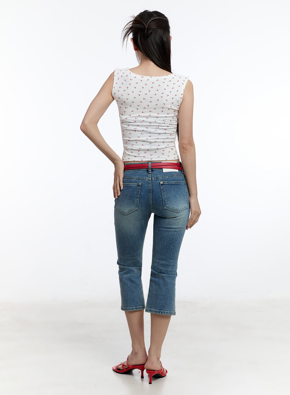 Kyra Cropped Low-Rise Skinny Jeans IU503 in blue, back full-body on model, washed denim showing back pockets and cropped hem with slight flare, red belt at low waist, red heeled sandals.