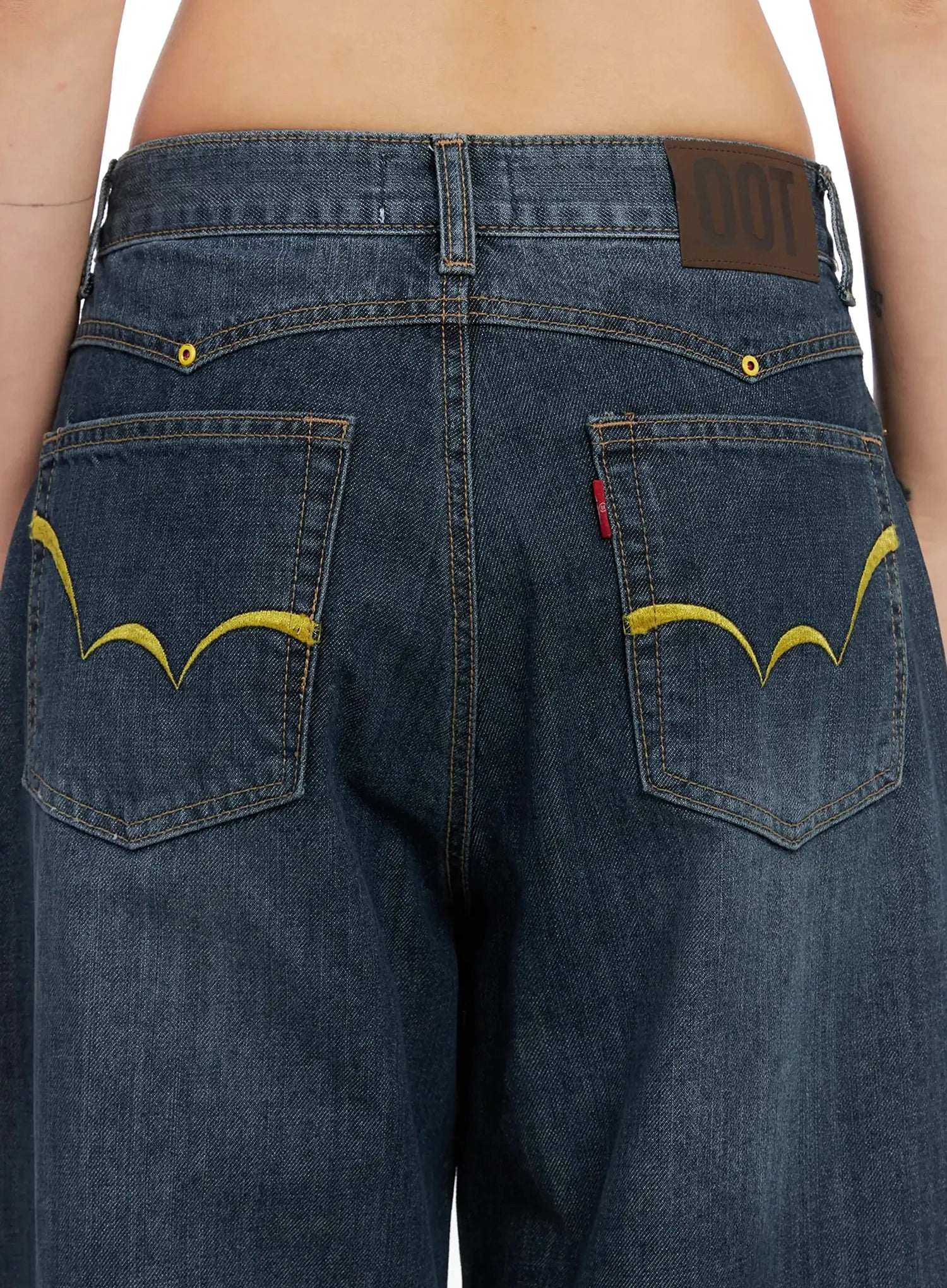 Regina Contrast Stitch Baggy Jeans IN528 in dark blue wash, back waistband close-up, yellow arc embroidery stitching on back pockets, brand leather patch label, yellow rivets on washed cotton denim.