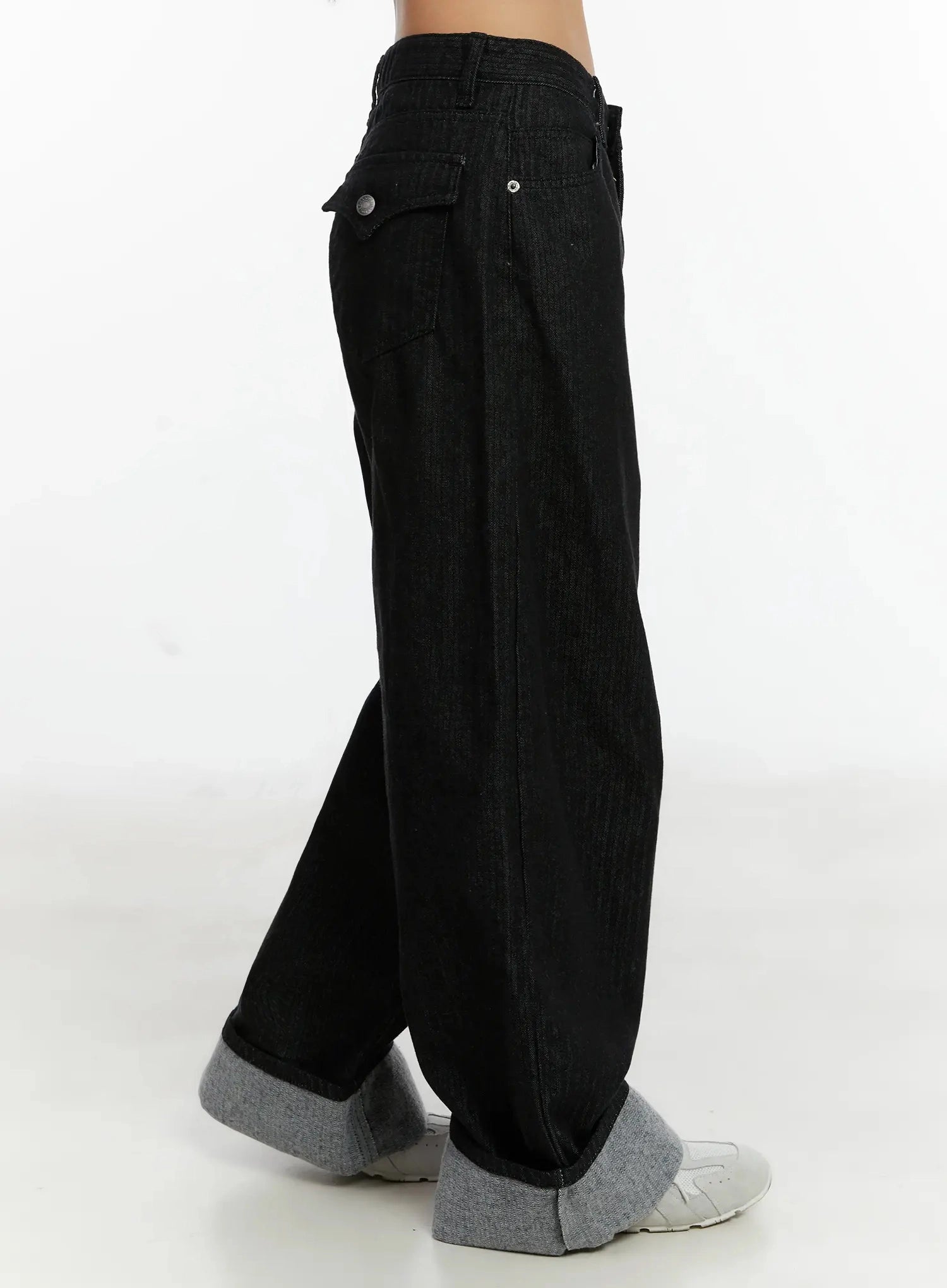 Amyra Baggy Striped Jeans ID525 in black, side close-up on model, highlighting rear flap pocket with button, vertical stripe cotton fabric, and voluminous leg with grey cuffed hem.