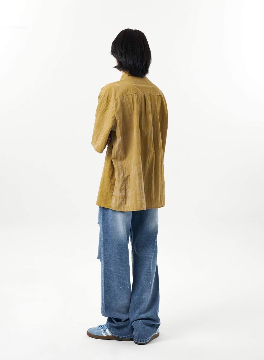 Ripped Jeans Unisex CU315 in mid blue, full-body back view on male model, wide-leg cotton denim with paint splatter and clean back panel, worn under olive crinkle shirt, relaxed tomboy silhouette.