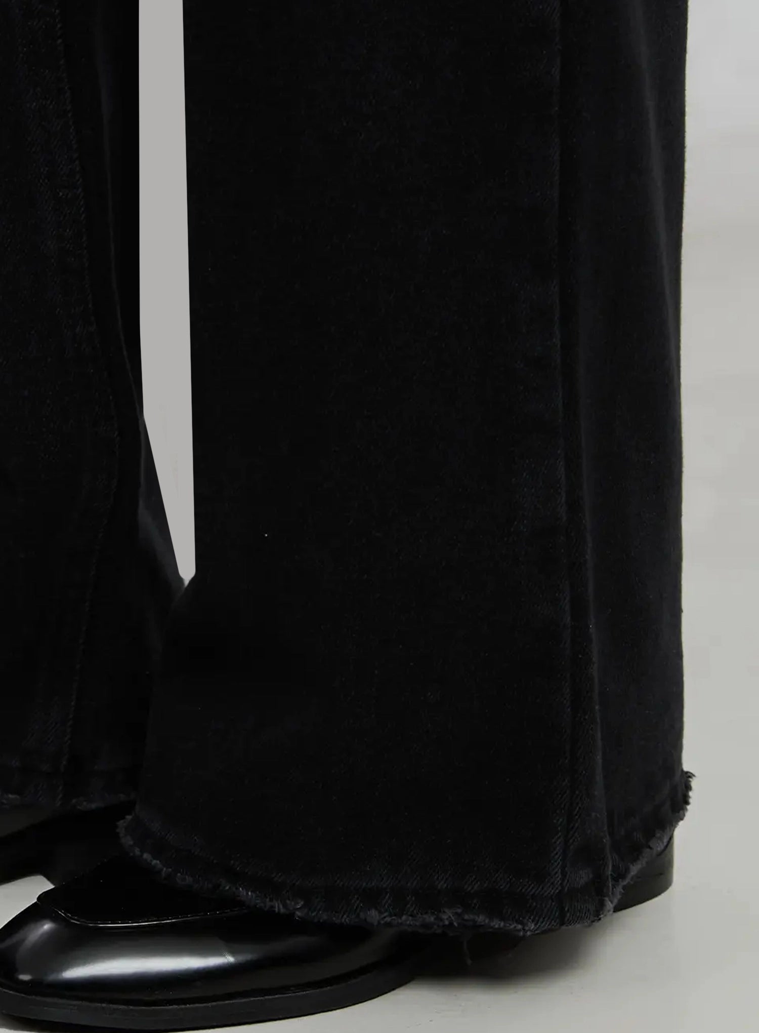 Imani Wide-Leg Flared Jeans ID516 in black, hem close-up detail, showing raw frayed edge of wide flared leg, cotton denim texture, and black pointed-toe loafer underneath.