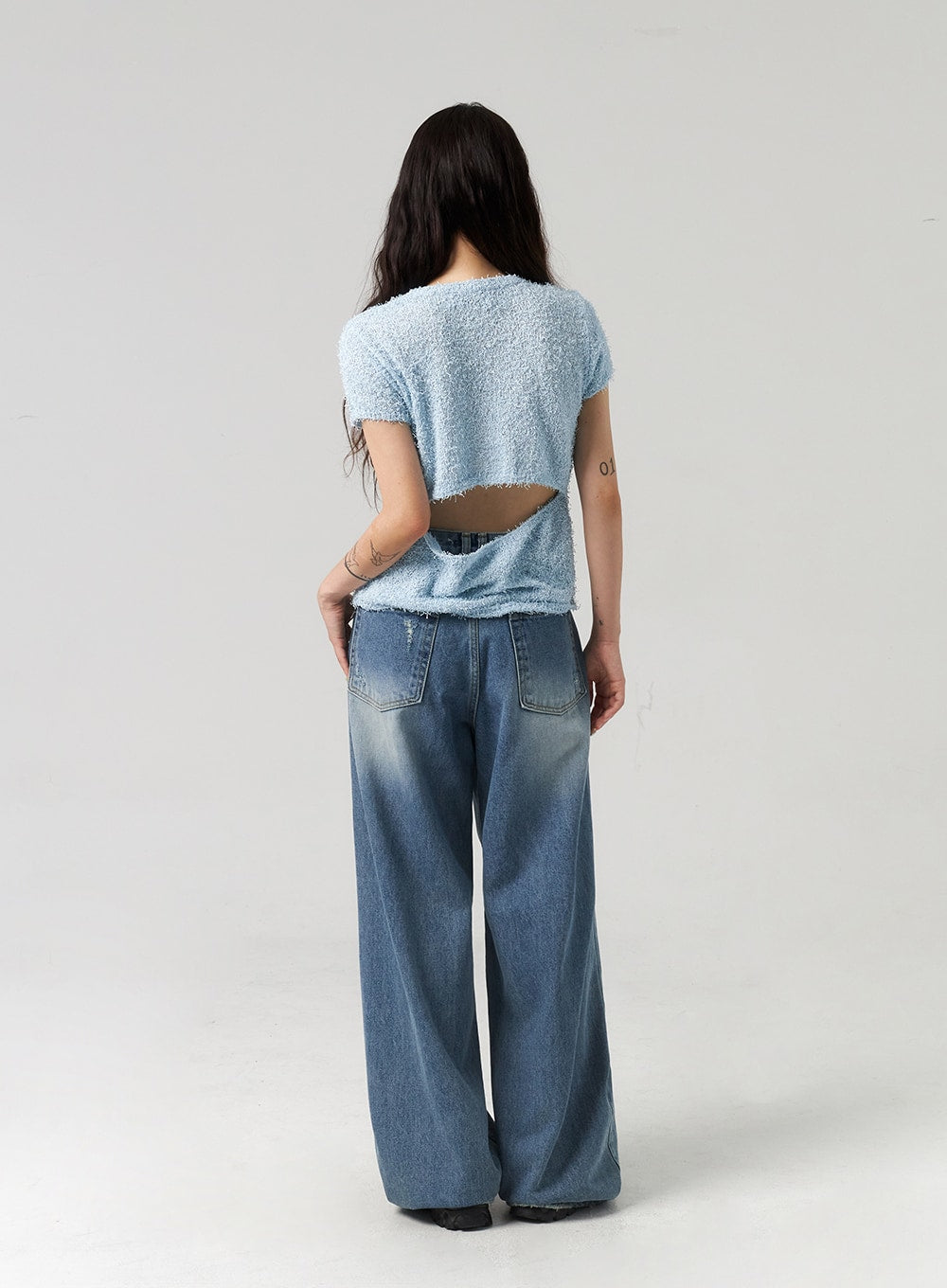 Baggy Jeans CL313 in washed blue, full-length back view on model, revealing wide-leg silhouette, back patch pockets with fading, long hem, paired with light blue open-back bouclé top.