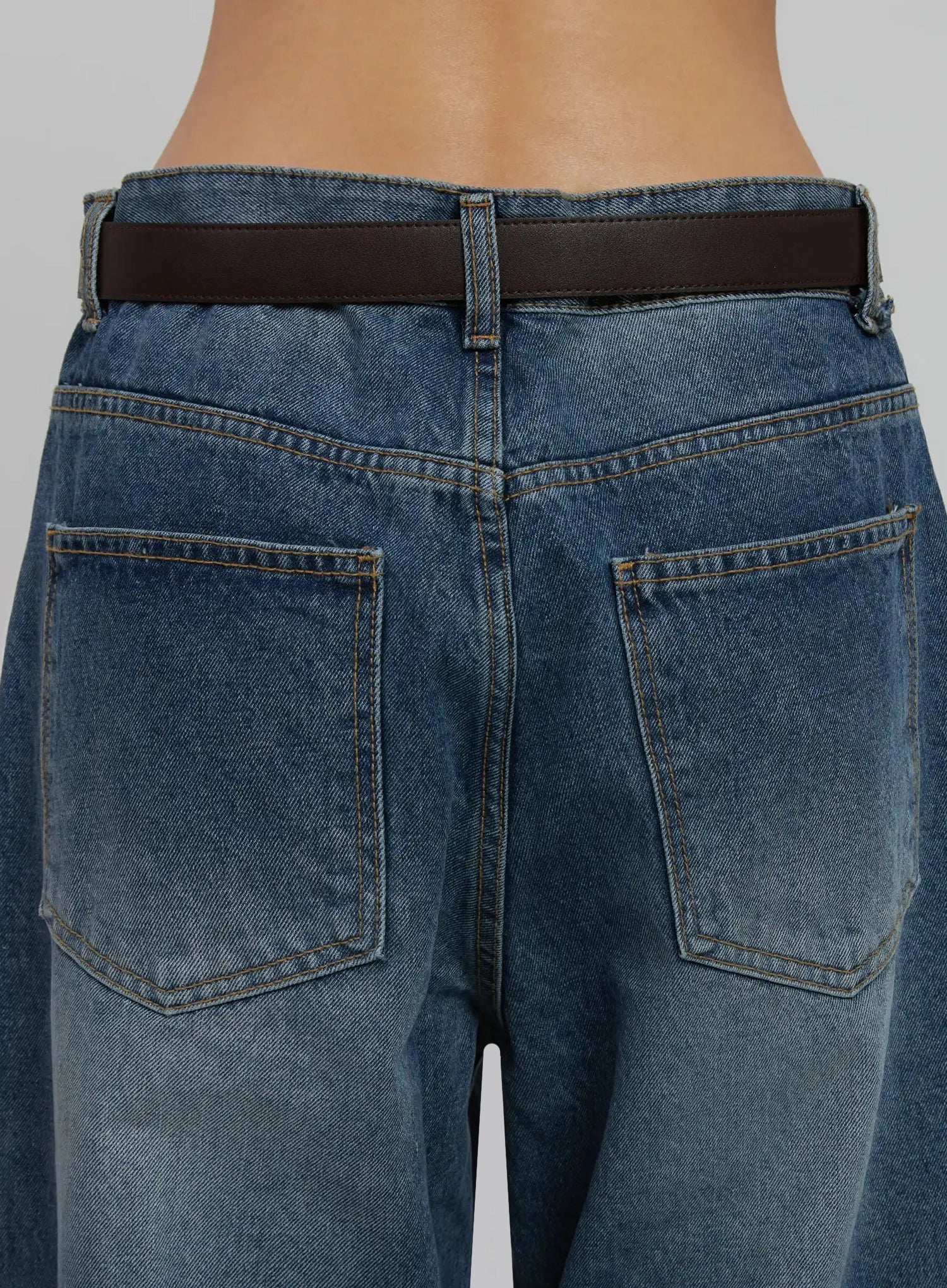 Akira Wide Leg Jeans IJ508 in blue, back waist close-up on model, showing back patch pockets, topstitching, washed denim texture, and brown belt detail.