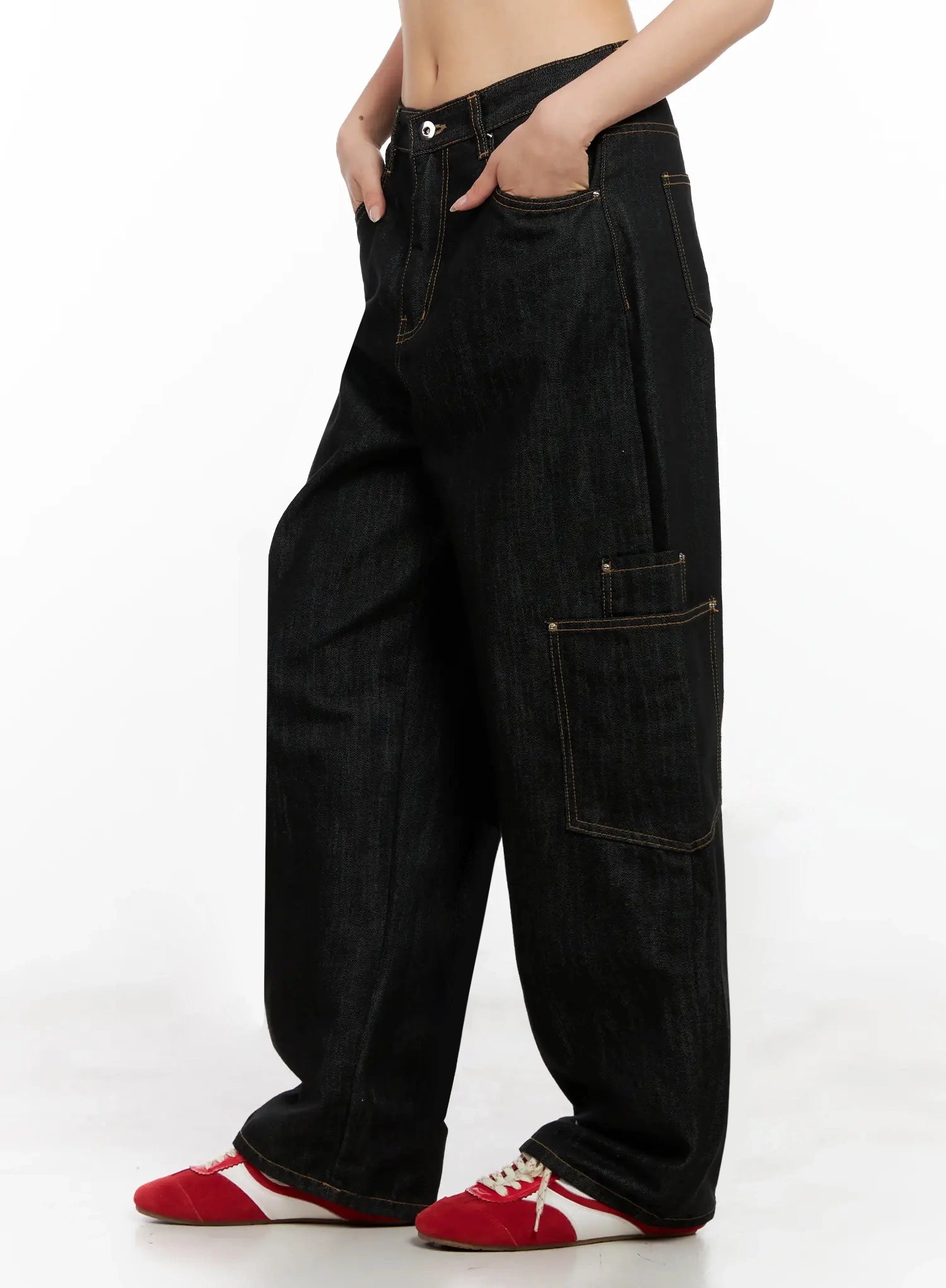Dahee Wide-Leg Cargo Jeans IG508 in black, side view on headless model hand in pocket, side cargo flap pocket and contrast gold stitching visible, voluminous wide-leg silhouette, styled with red sneakers.
