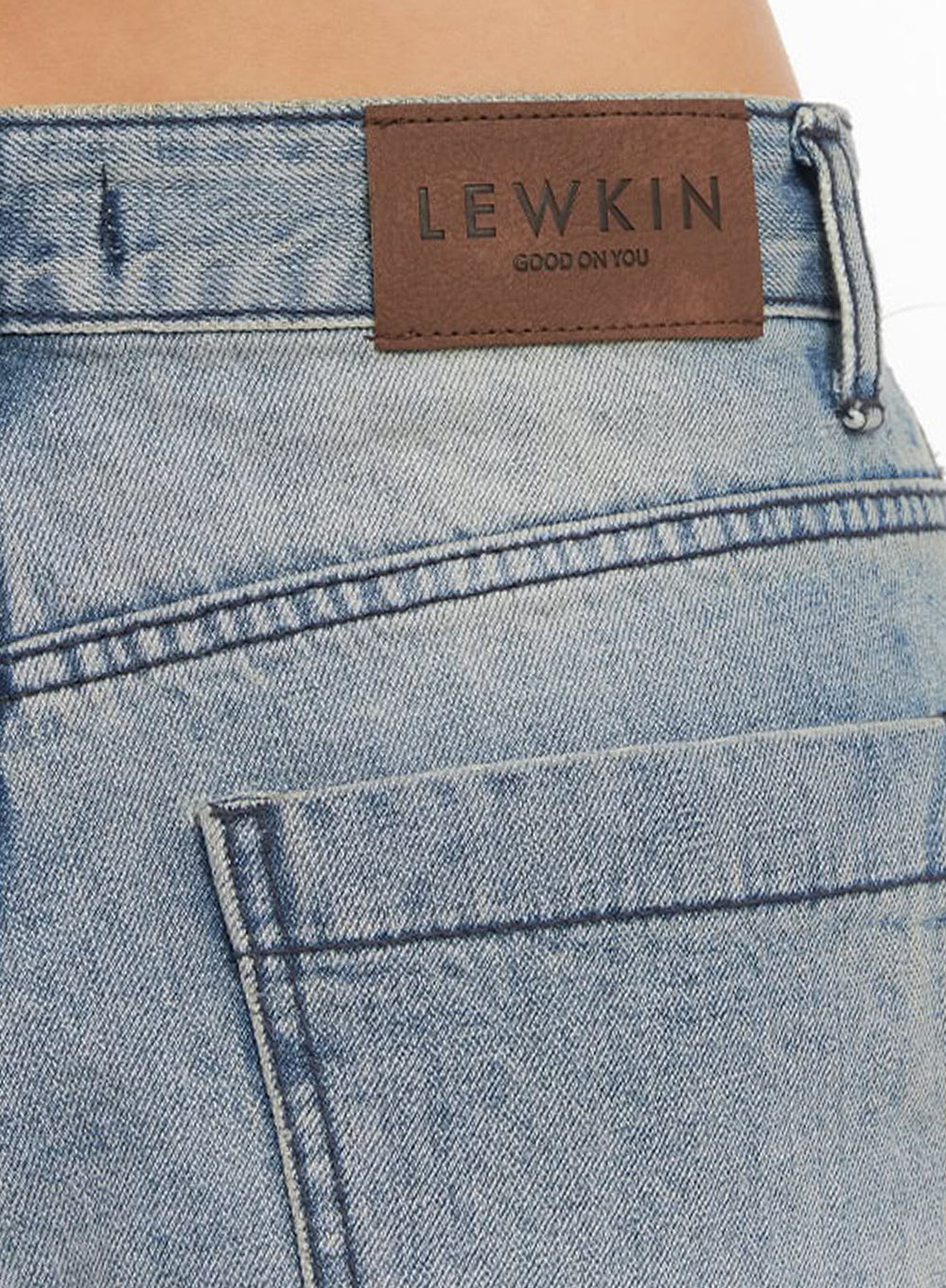 Casey Washed Baggy Jeans IM528 in light blue, macro close-up of back waistband, brown leather LEWKIN logo patch with contrast stitching on washed denim, belt loop and back pocket detail.