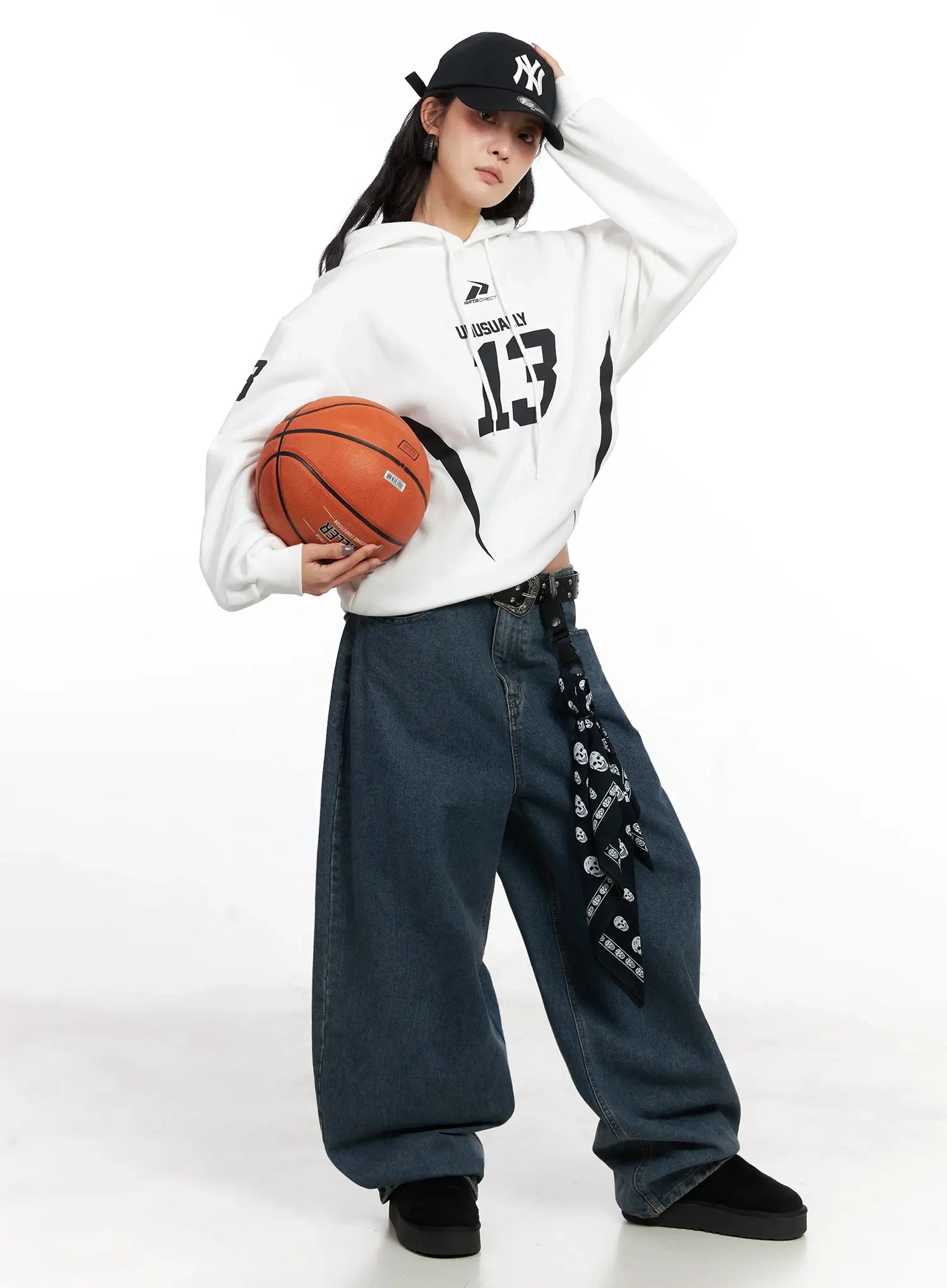 Aleena Mid-Wash Baggy Jeans IN528 in dark blue, full-length front shot on model holding basketball, styled with white graphic hoodie, NY cap and skull-print belt, sporty street look.