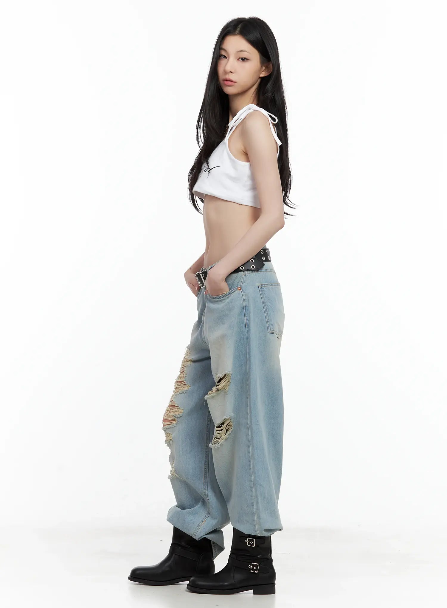 Gyuri Dirty-Wash Distressed Wide Jeans CU530 in blue, side profile on model, low-rise wide fit with thigh distressing, black studded belt, white crop halter top and black boots.