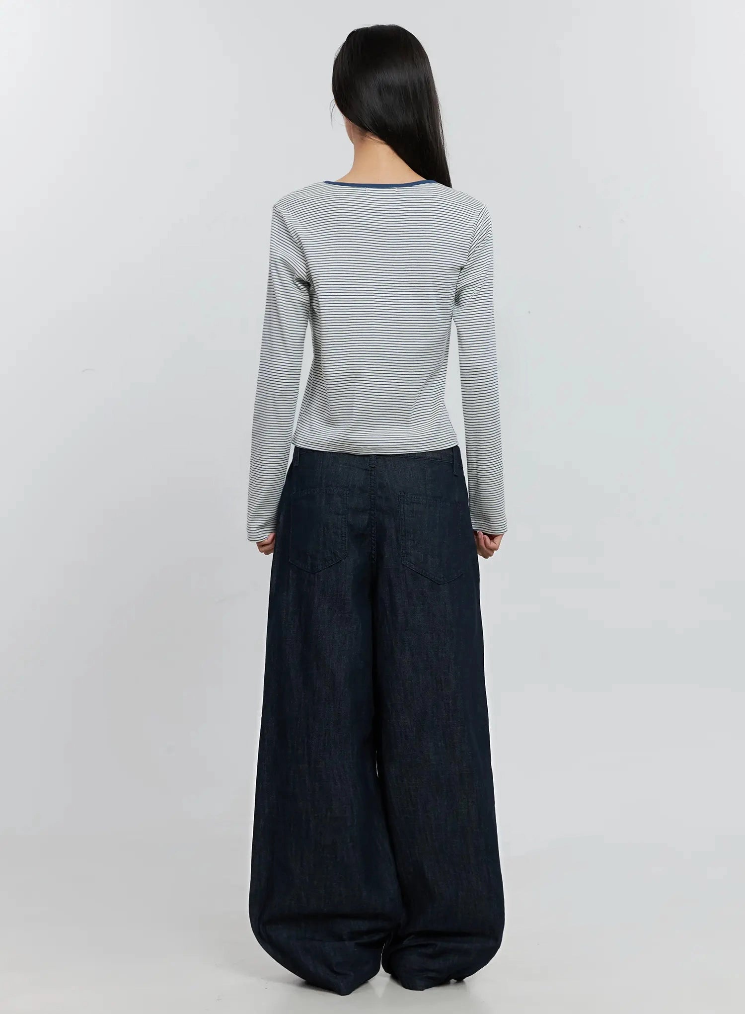 Elio Pintuck Wide-Leg Jeans IS516 in dark indigo, back full-length on model, patch pockets and sweeping wide leg visible, paired with white striped long-sleeve crop top.