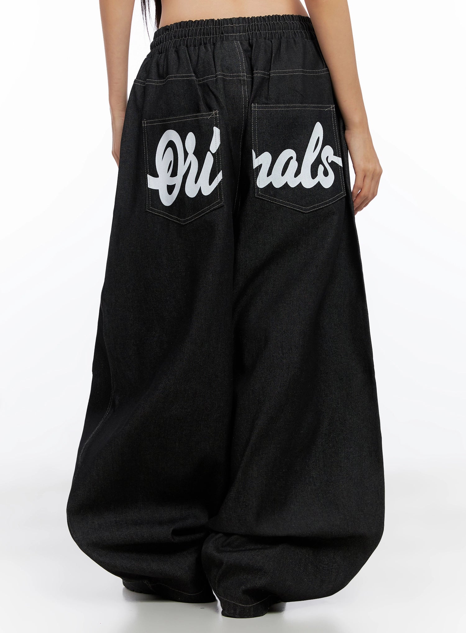Ayra Graphic Baggy Jeans IO516 in Black, back mid-shot on model, oversized balloon leg in cotton denim, bold cursive Originals lettering spanning dual banded pockets, elastic waistband.