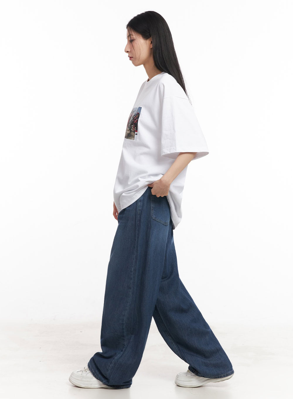 Martha Baggy Jeans IY529 in dark blue, full side-profile shot on model mid-stride, wide-leg washed denim with sweeping hem, paired with white oversized graphic tee and white sneakers.