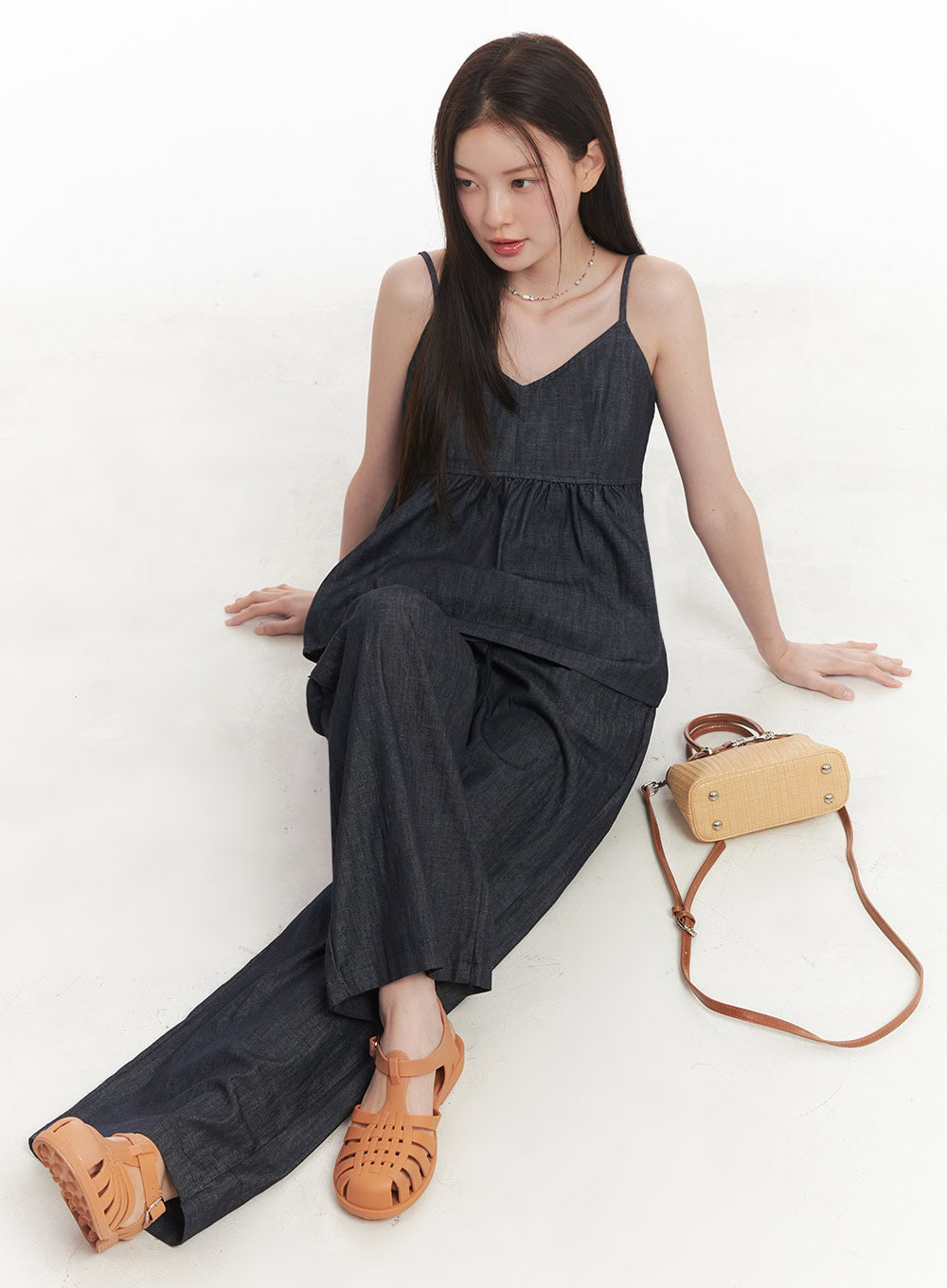 Cotton Denim Wide-Leg Pants IY509 in dark navy, seated lifestyle shot on model, wide-leg cotton denim pooling at feet, styled with denim cami top, tan sandals, and straw mini crossbody bag.