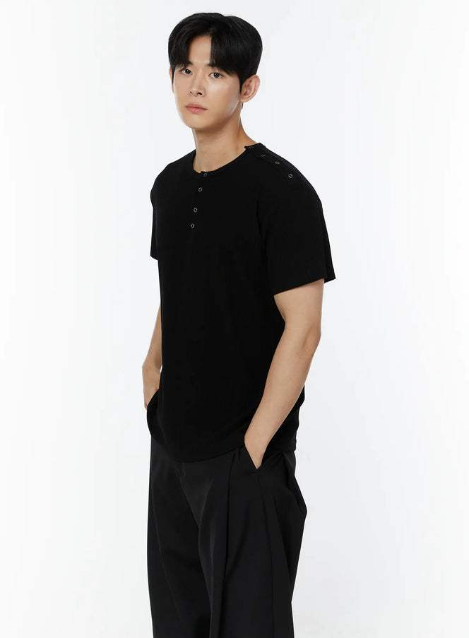 LEWKIN Men's Ribbed Snap Shoulder Henley T-Shirt IU508 in black, 3/4 front view on model, ribbed short sleeve with henley snap placket and snap shoulder detail, paired with black wide-leg trousers.