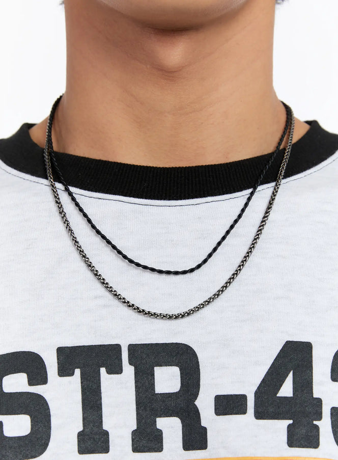 LEWKIN Dual Chain Necklace IN524 in Black, front close-up on model's neck, layered twisted cord and wheat-link chains, worn over white graphic tee.
