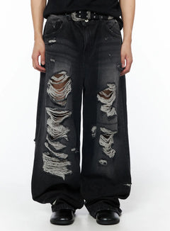LEWKIN Men's Vintage Distressed Baggy Jeans (Black) IU510 in black, front close-up on model, extreme heavy distressing with frayed denim tears on thighs, ultra-wide leg silhouette, styled with studded western belt.