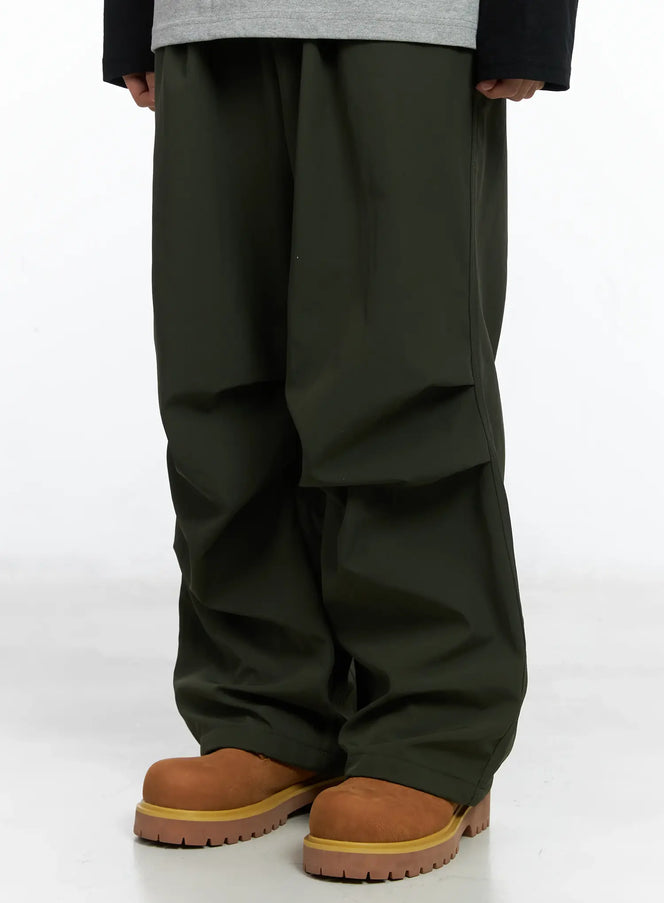 LEWKIN Men's Fleece Parachute Pants IN518 in dark green, front close-up on model, wide-leg silhouette with layered paneling, paired with tan boots.