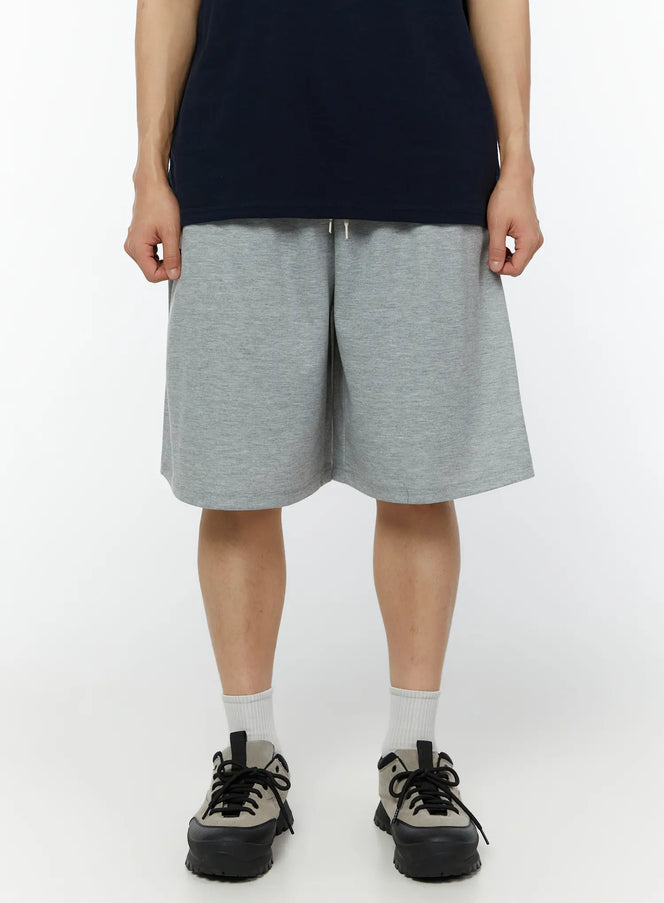 LEWKIN Men's Basic Bermuda Sweat Shorts IU515 in gray, front view on model, relaxed wide-leg sweat shorts with drawstring waist, paired with navy tee and chunky sneakers.