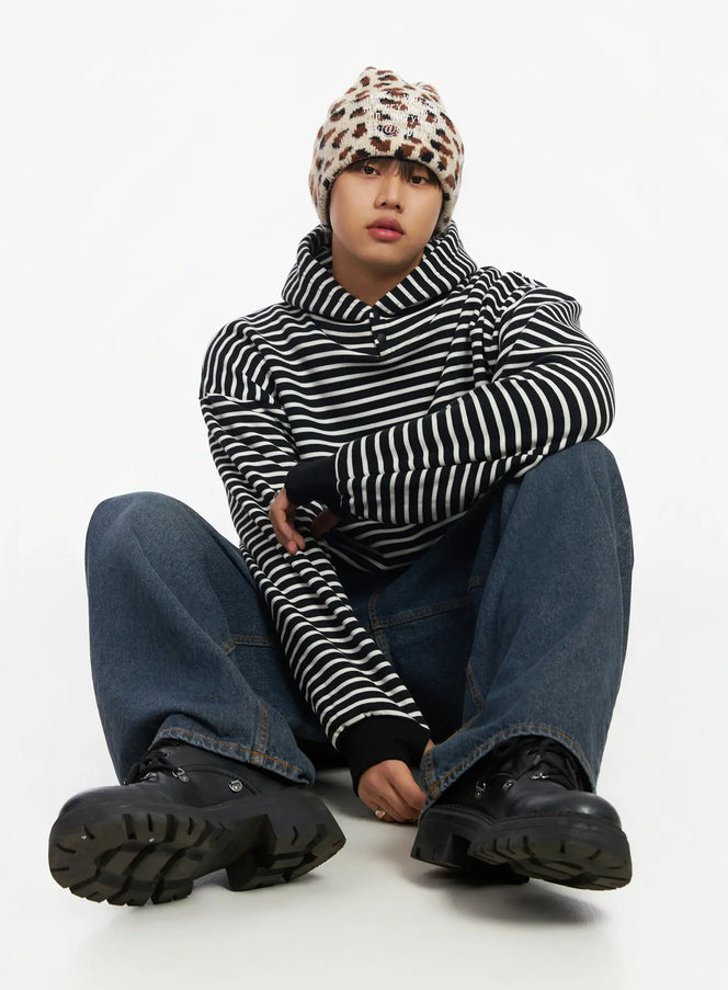 LEWKIN Men's Striped Button Neck Hoodie IF503 in black and white, editorial seated pose on model, arms crossed, oversized fit with high neck, styled with leopard beanie and wide-leg jeans.