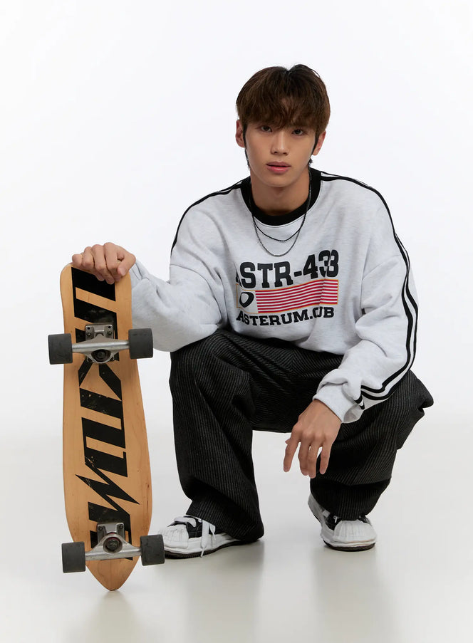 Dual Chain Necklace IN524 in Black, full-body styling shot on crouching male model, dual layered chains visible at neckline, paired with grey sweatshirt and dark wide-leg pants.