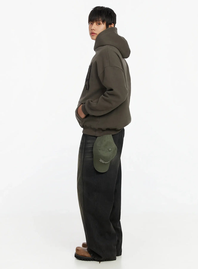 Men's Patch Stitch Fleece Hoodie IF503 in dark olive, side full-body view on model, oversized drop-shoulder fleece hoodie, styled with wide-leg dark jeans, brown boots, and a green cap.
