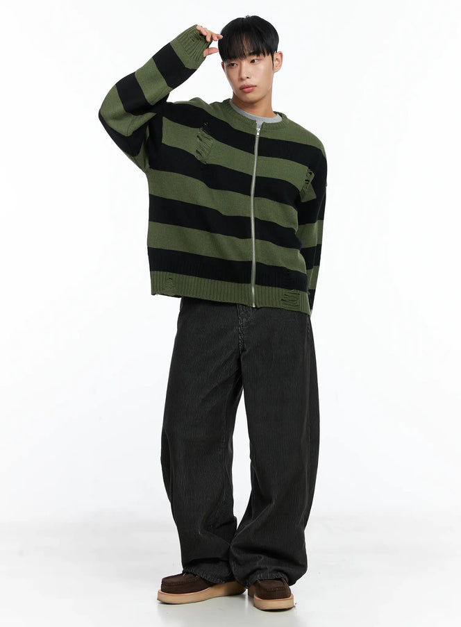 Men's Stripe Distressed Knit Cardigan IN518 in green, full-body shot on model with hand raised, oversized fit, green-black stripe knit, distressed details, styled with wide-leg dark corduroy pants and brown shoes.