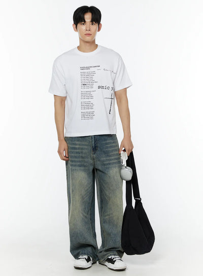 Men's Adan Baggy Washed Jeans IU508 in blue, full-body front on model, oversized washed denim with horizontal crease lines, styled with white graphic tee, black tote bag with headphones, and white sneakers.