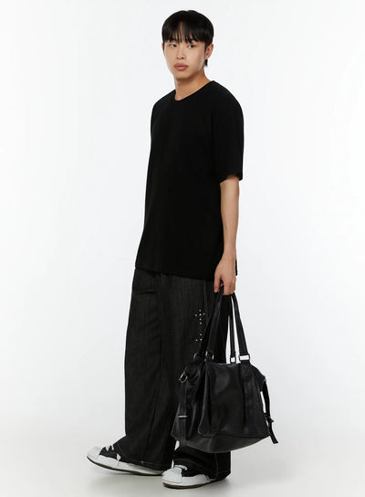 Men's Wide Leg Jeans IU515 in black, full-length side view on male model, ultra-wide leg, stud cross accent, paired with long black tee and black duffel bag, high-top sneakers.