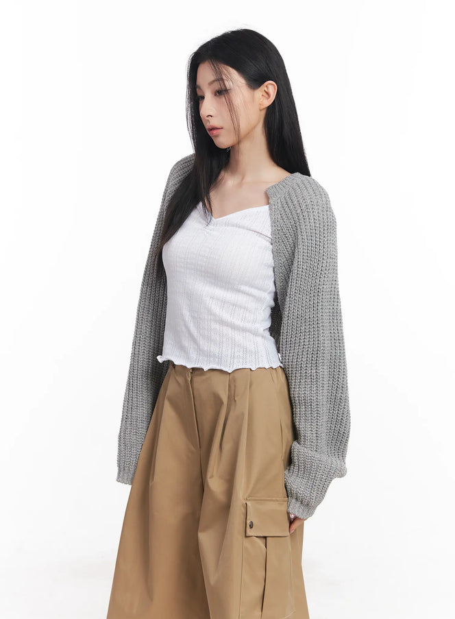 LEWKIN Knit Bolero Shrug C2001 in grey, 3/4 side view on model, open-front cropped chunky knit shrug with balloon sleeves, layered over white ribbed top and khaki cargo trousers.