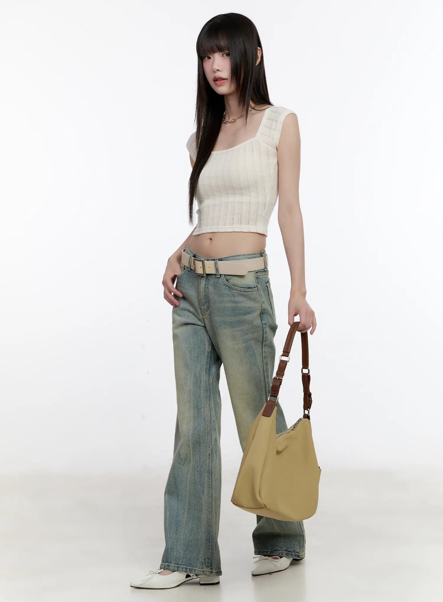 Roa Vintage Blue Flared Denim Jeans CL504 in blue, full-body side-angled shot on model holding tote bag, low-rise washed bootcut denim with beige belt, cream knit crop top, white flats.