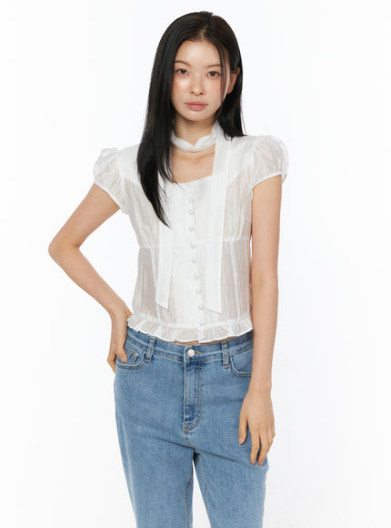 Puff Sleeve Shirred Blouse with Scarf IU519 in white, front view on model with hand on hip, lightweight sheer nylon-tencel fabric with shirring and ruffled hem, scarf accent, with blue jeans.