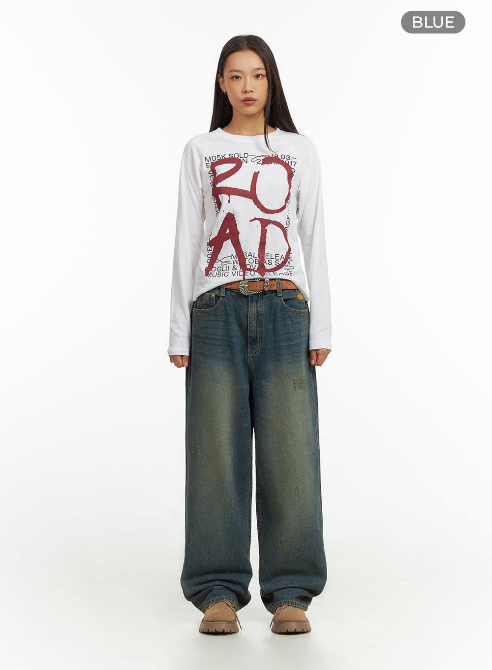 Anya Wide Fit Denim Jeans IO409 in blue, full-body front view color reference shot on model, baggy washed cotton denim with vintage fade and distressing, styled with white graphic tee and brown western belt.